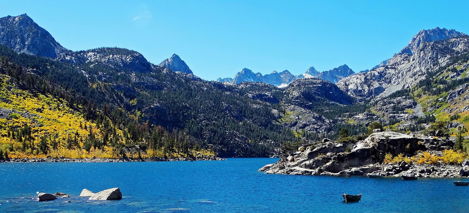 A deep blue mountain lake below granite peaks, with aspens in yellow along the slope on the left.
