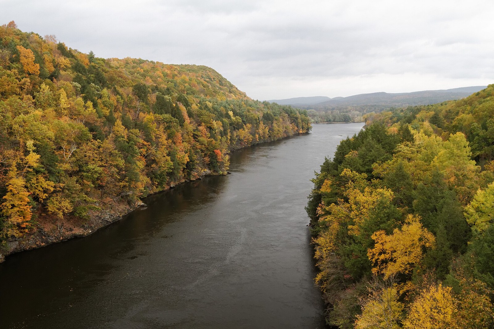 The Connecticut River running between wooded hills in yellow, orange and green.