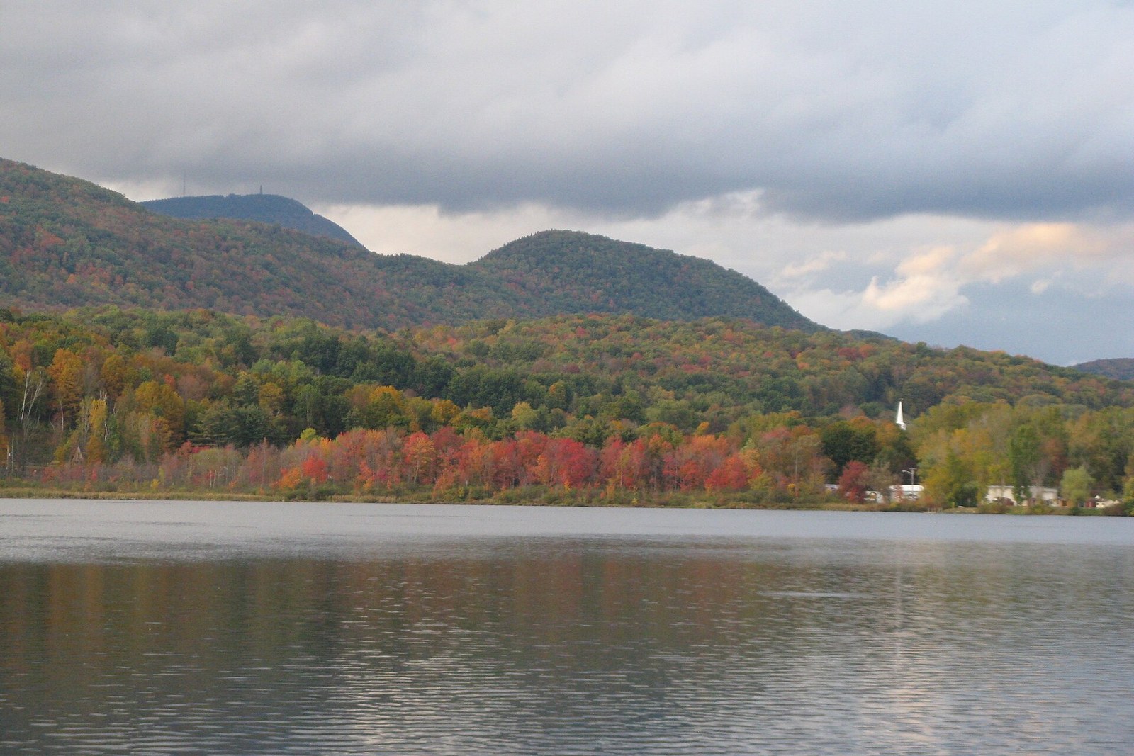 A calm reservoir below wooded hills, a band of red trees along the shore and Mount Greylock behind.