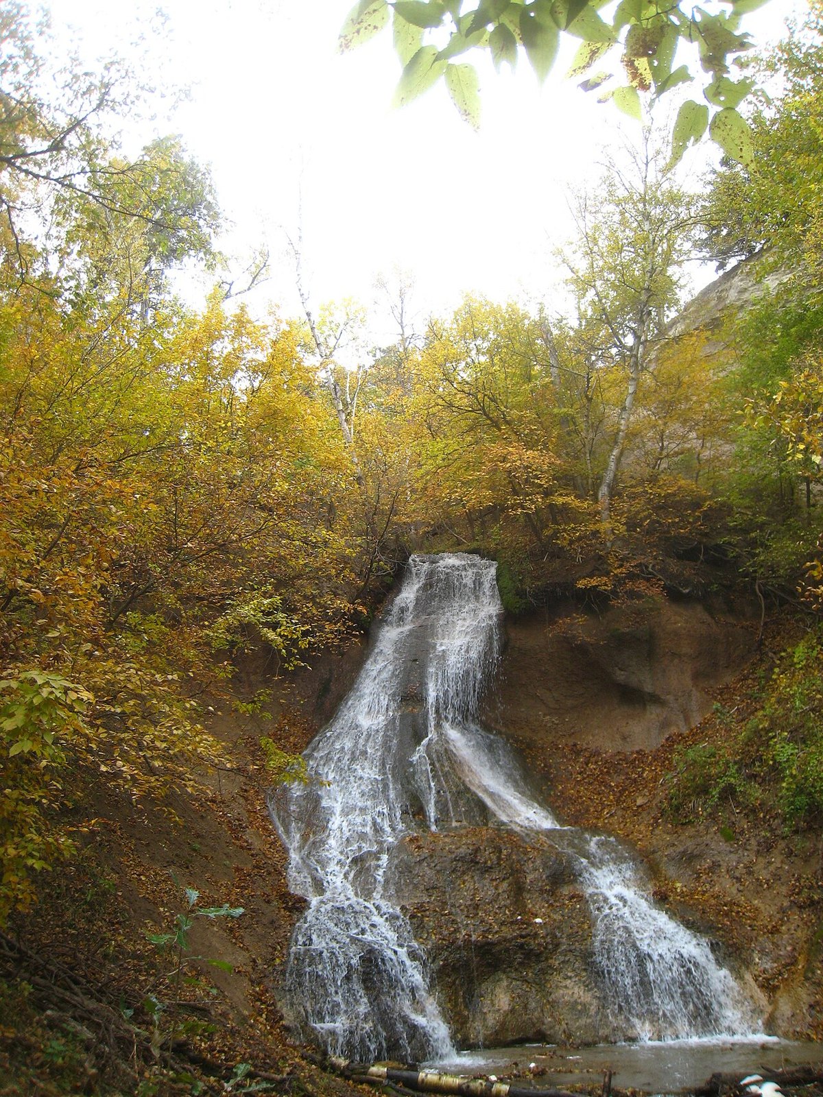 A waterfall tumbling down a rocky bank among birch and other trees in yellow and orange leaves.