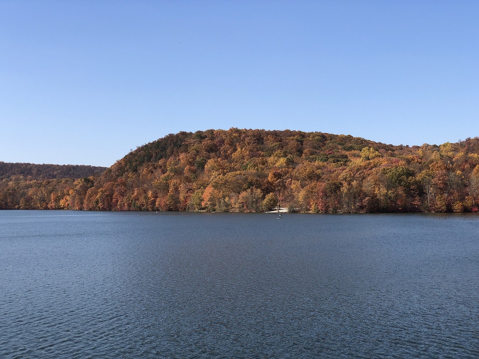 A rounded wooded hill in orange and rust seen across a dark reservoir.