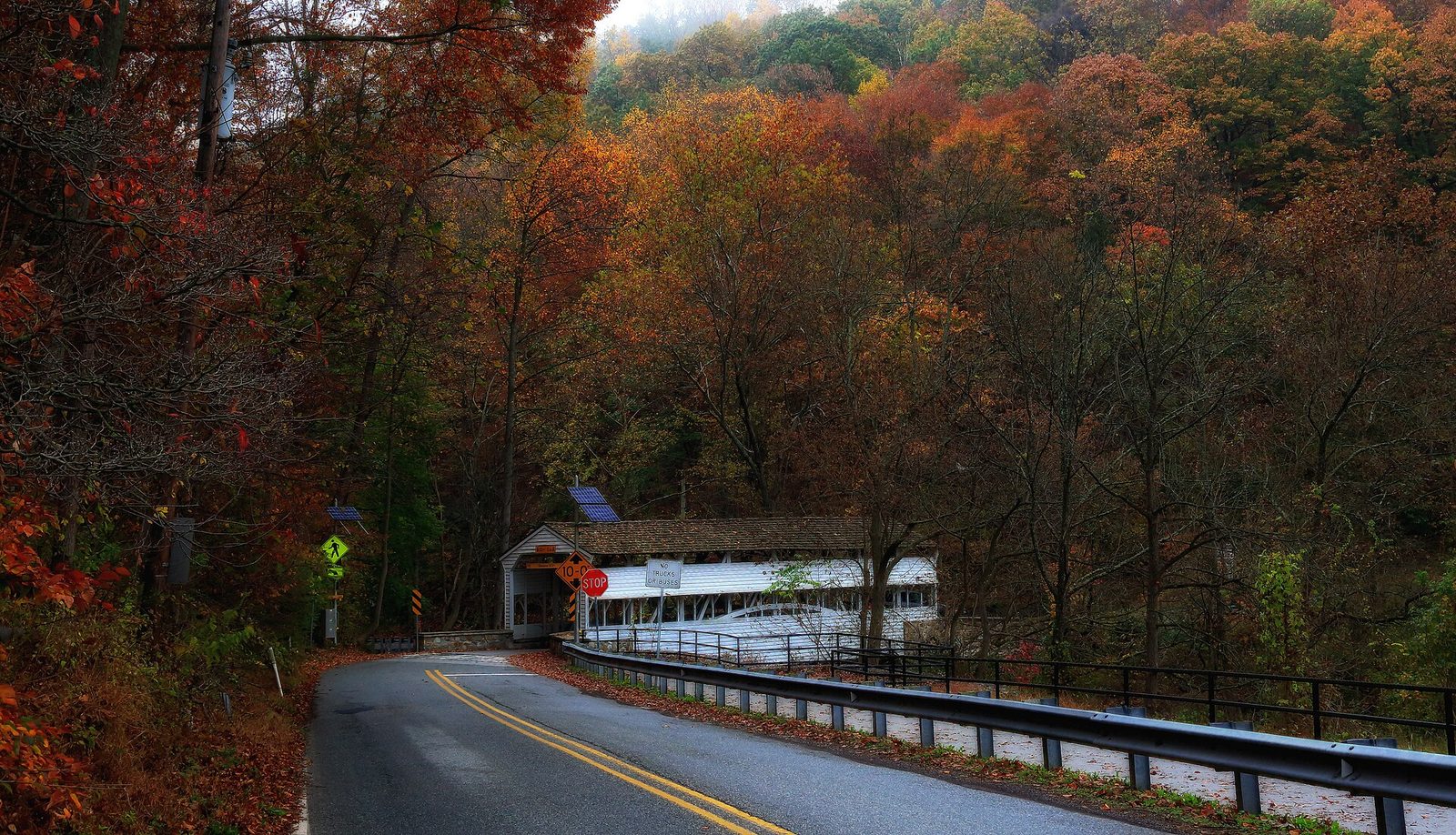 A white covered bridge beside the road at Valley Forge, with hillsides of red and orange trees behind it.