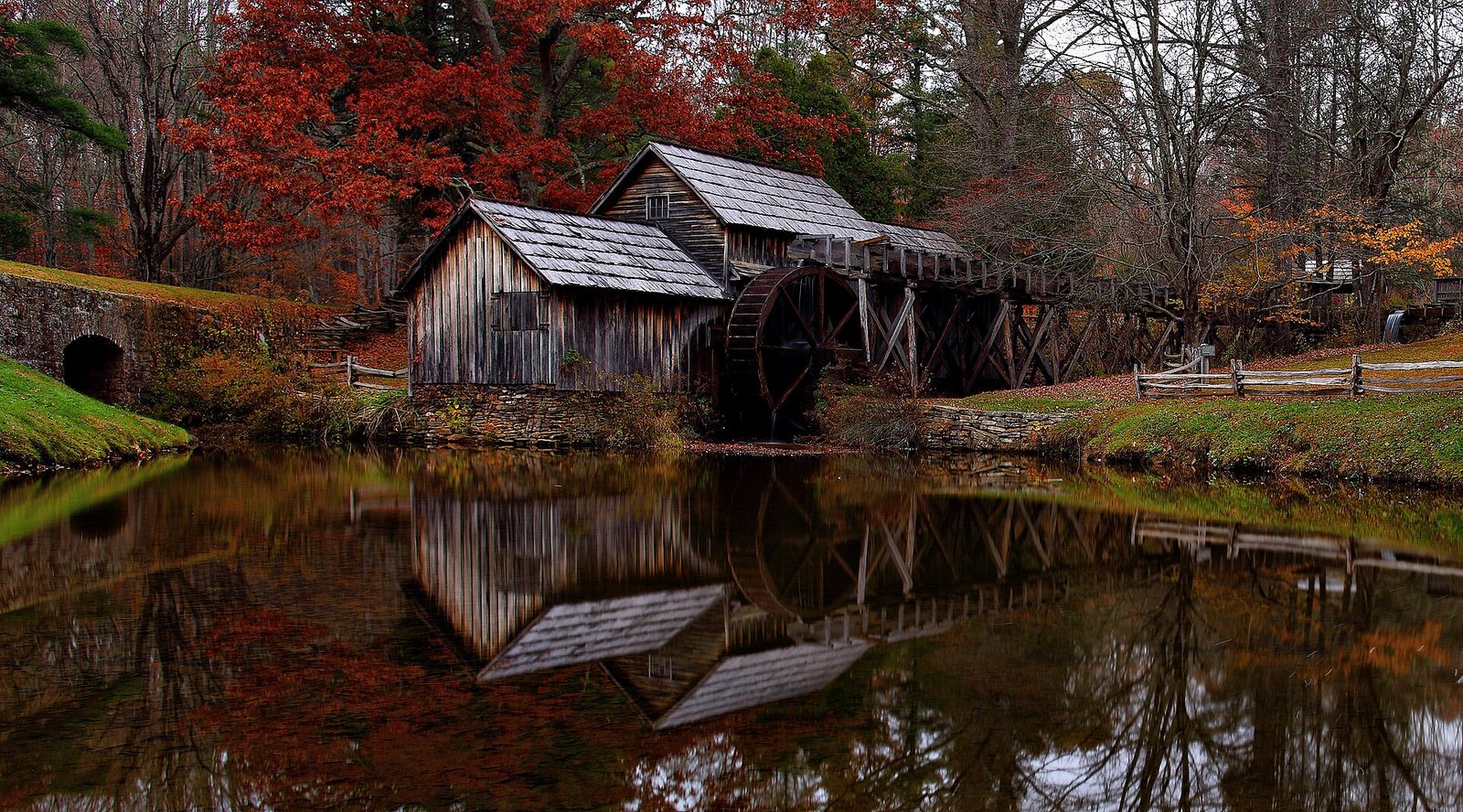 Mabry Mill and its wheel reflected in a still pond, with red and orange trees behind.