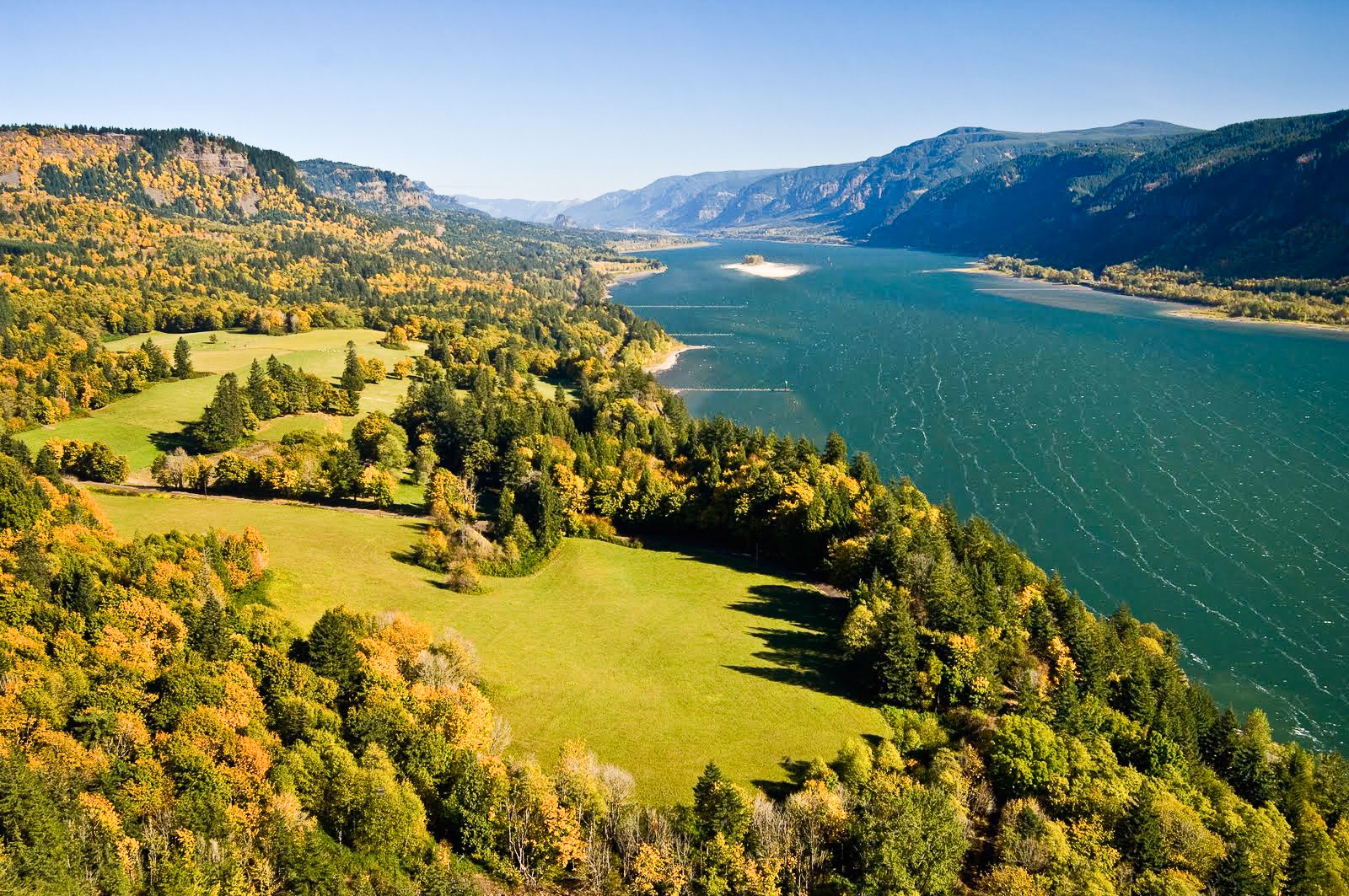 The Columbia River winding between steep slopes in autumn gold and green, seen from a high overlook.