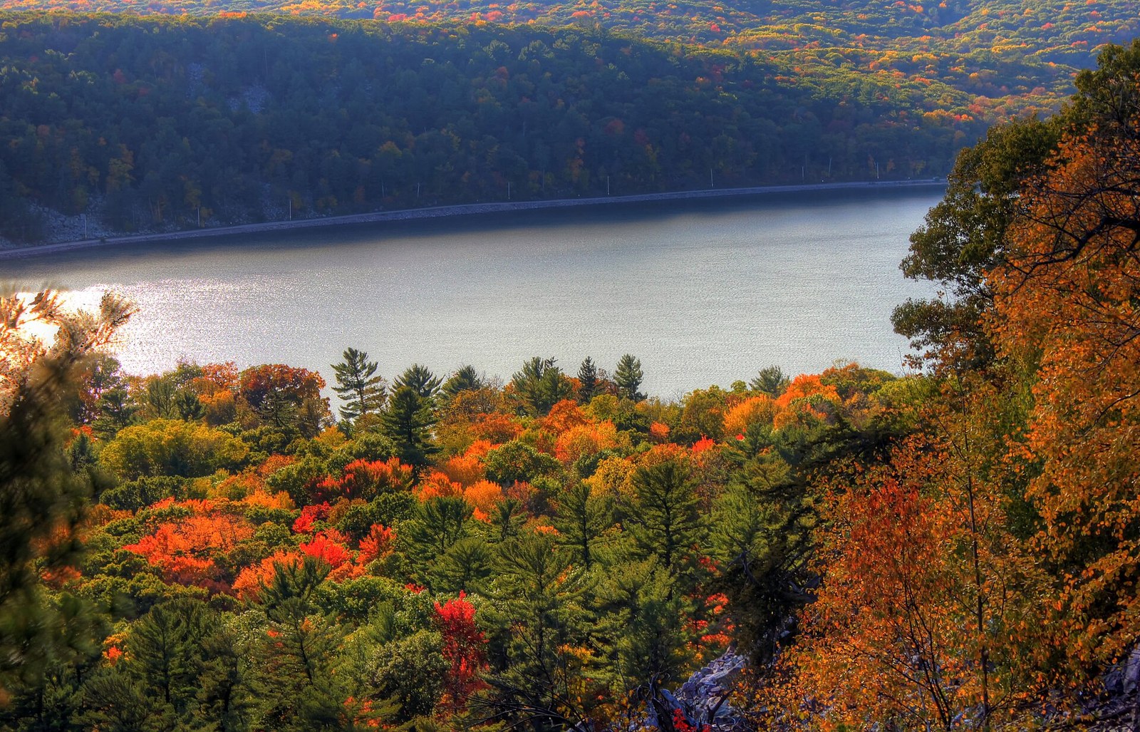 Orange and red trees in the foreground above a wide lake, with a forested bluff on the far shore.